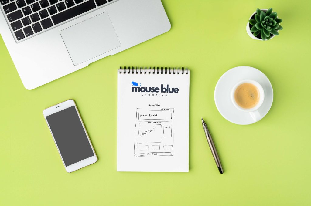 Small business website design strategy sketch on notepad with laptop, phone, and coffee on desk.